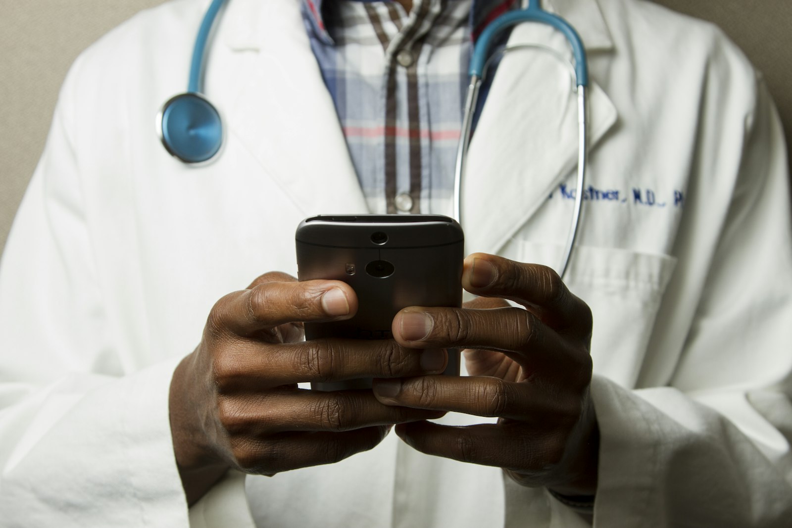 A UK doctor in a white coat with a stethoscope, using a phone to consult